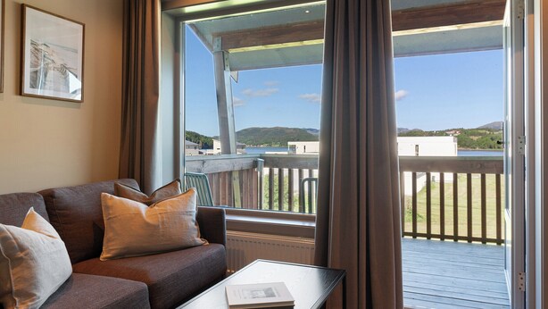A modern living room with a sofa, a coffee table, and a view of a balcony with a railing. - Bjugn Hotell (Orland)
