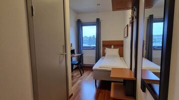 A hotel room with a bed, a desk, a chair, a mirror, and a window with a view of the outside.