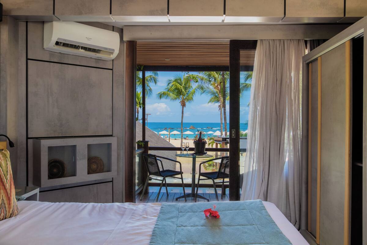 A hotel room with a bed, a small table with chairs, and a view of the beach and ocean.