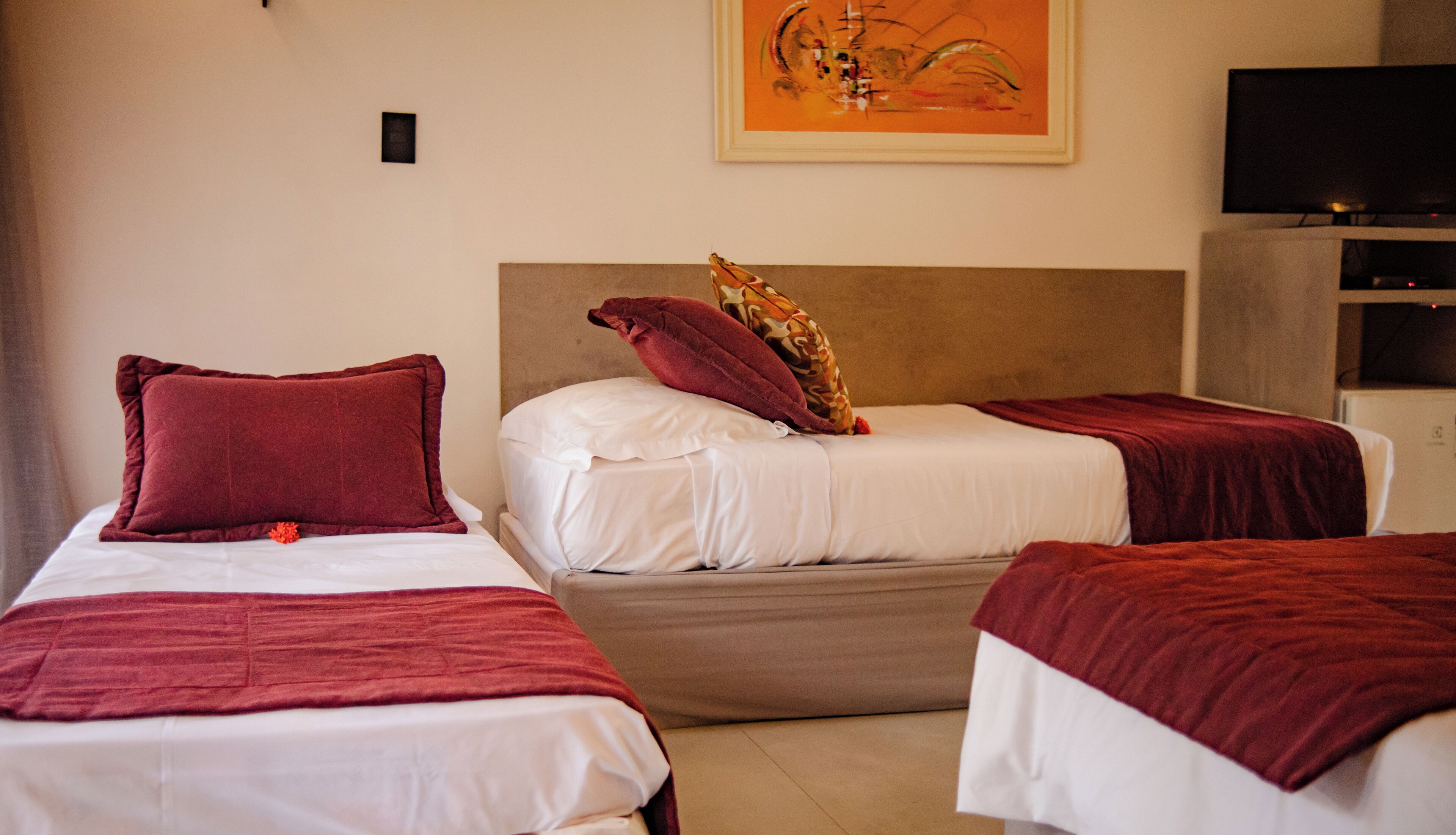 Une chambre d’hôtel avec deux lits simples, chacun recouvert d’une couverture et doté d’un oreiller rouge, et un grand tableau accroché au mur.