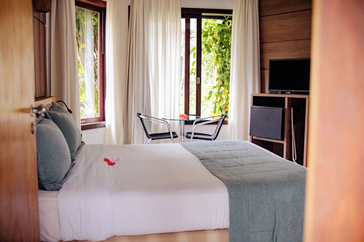A hotel room with a bed, a small table, chairs, a TV, and a window with curtains.