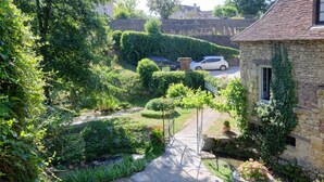 Ein Haus aus Stein mit Efeu, ein Garten mit einem Weg und geparkte Autos.