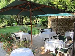 An outdoor patio with tables and chairs, a stone wall, and a green umbrella. - Logis Hôtel Le Moulin de la Beune (Les Eyzies)