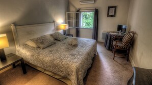 Ein Schlafzimmer mit Bett, Nachttischlampe, Fenster, Stuhl und einem kleinen Tisch mit Lampe.