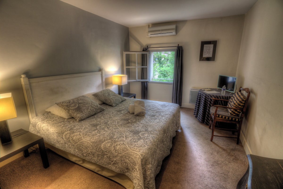 A bedroom with a bed, bedside lamp, window, chair, and a small table with a lamp.