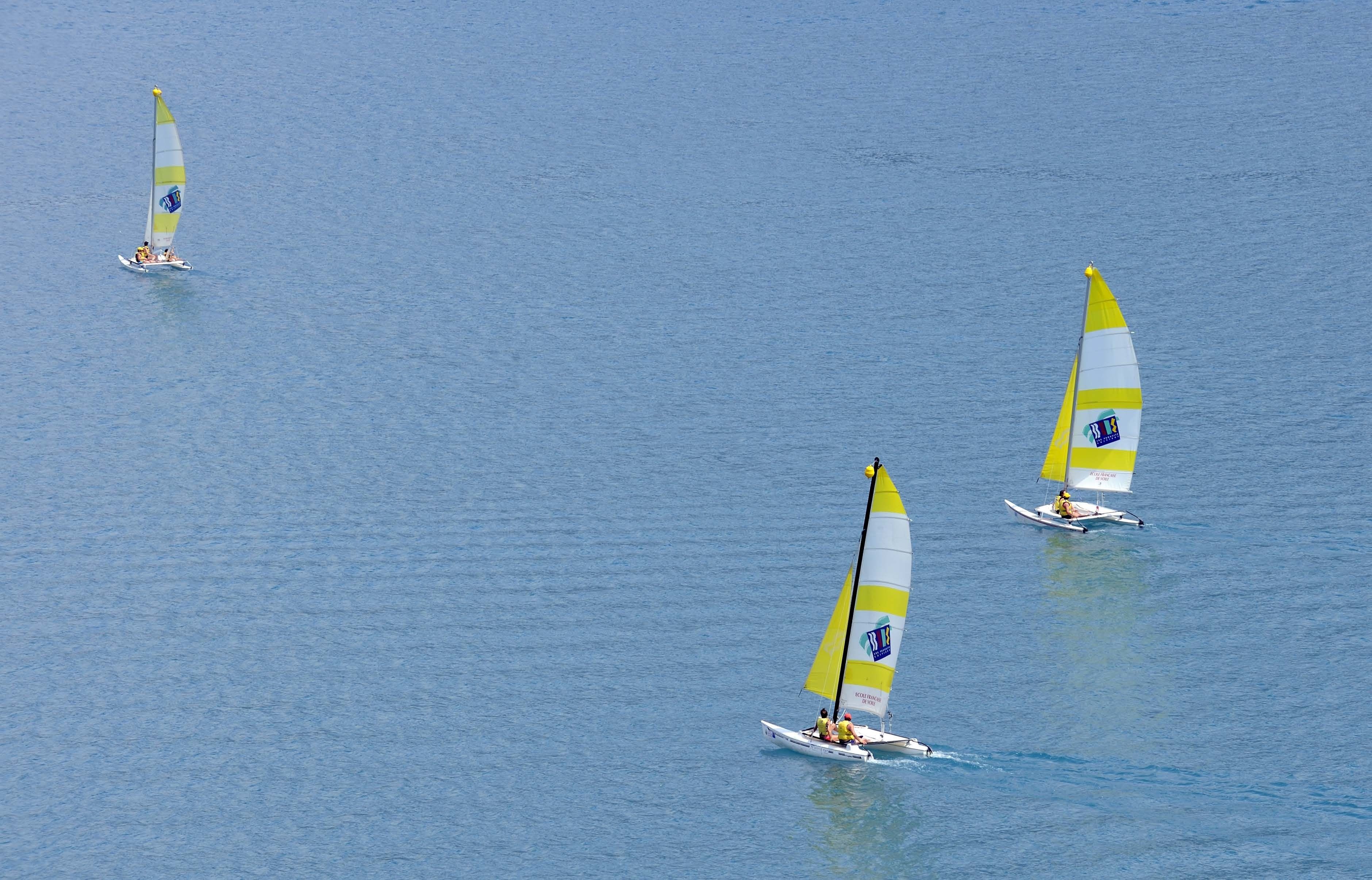 Three sailboats on a calm body of water.