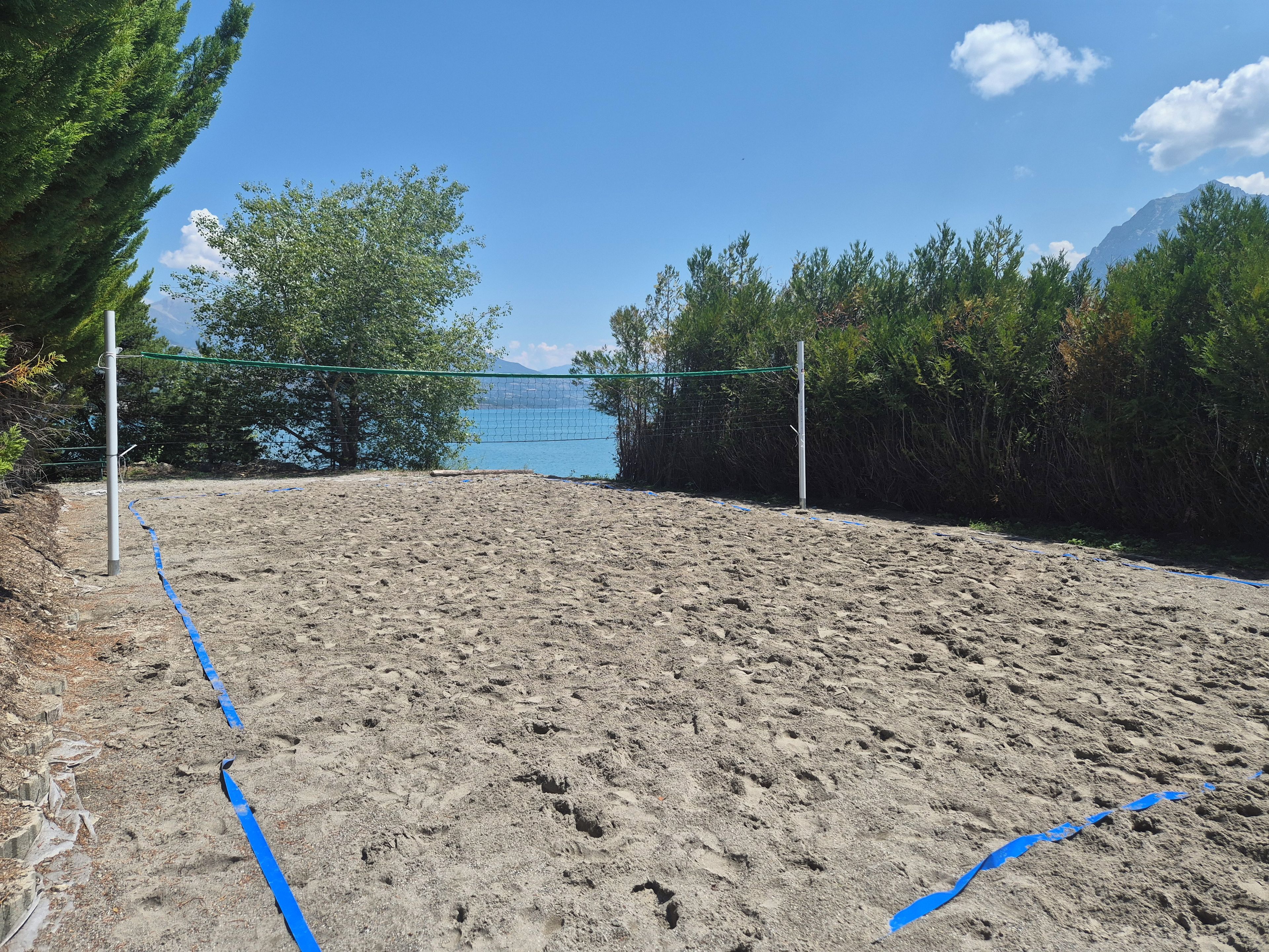 A sandy beach volleyball court with a net, surrounded by trees and a mountain in the background.