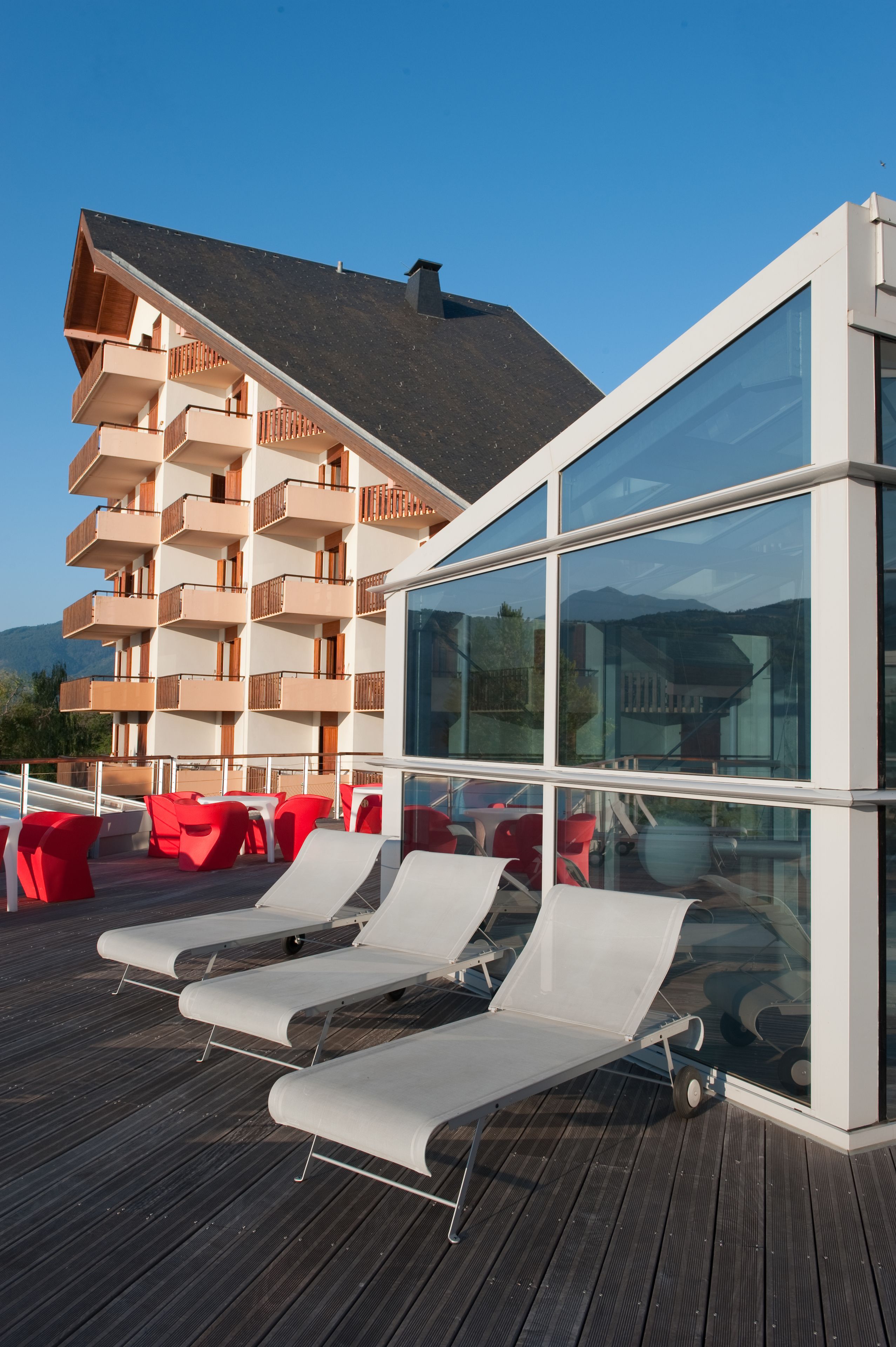 Un edificio moderno con facciata in vetro e terrazza in legno con poltrone relax.