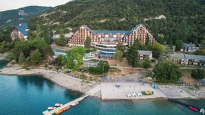 A hotel with a traditional European architectural style, located near a body of water with a dock and boats. - Village Club les Hyvans (Chorges)