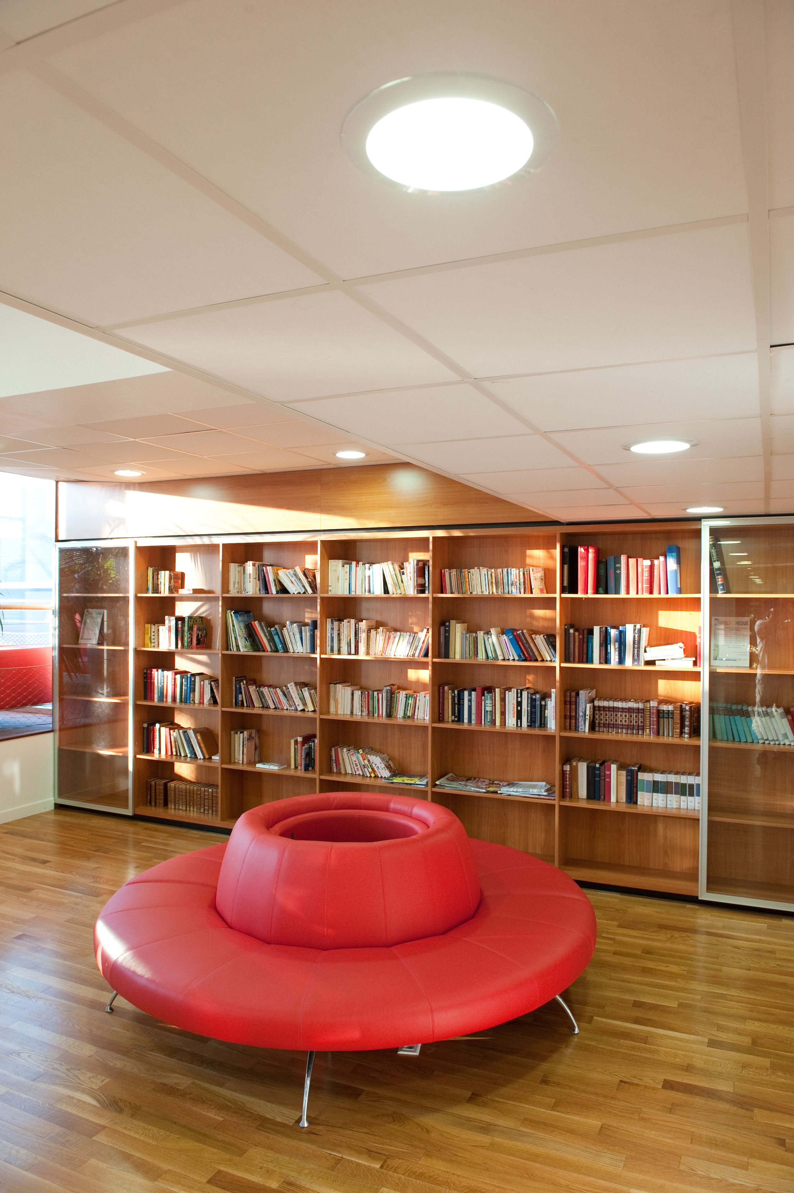 Una biblioteca con estanterías de madera y una zona de asientos circular en rojo.