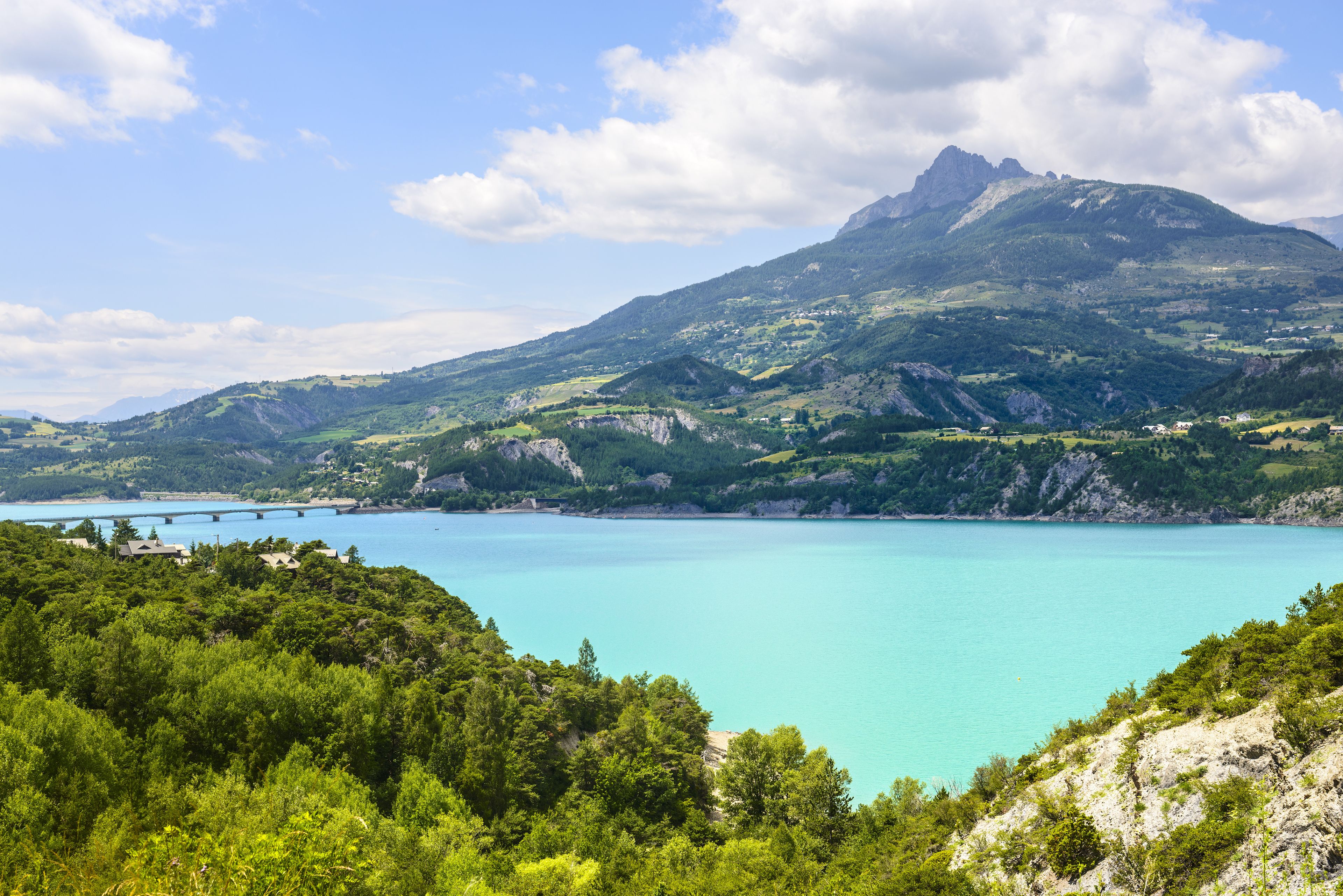 A mountainous landscape with a turquoise lake and a bridge.