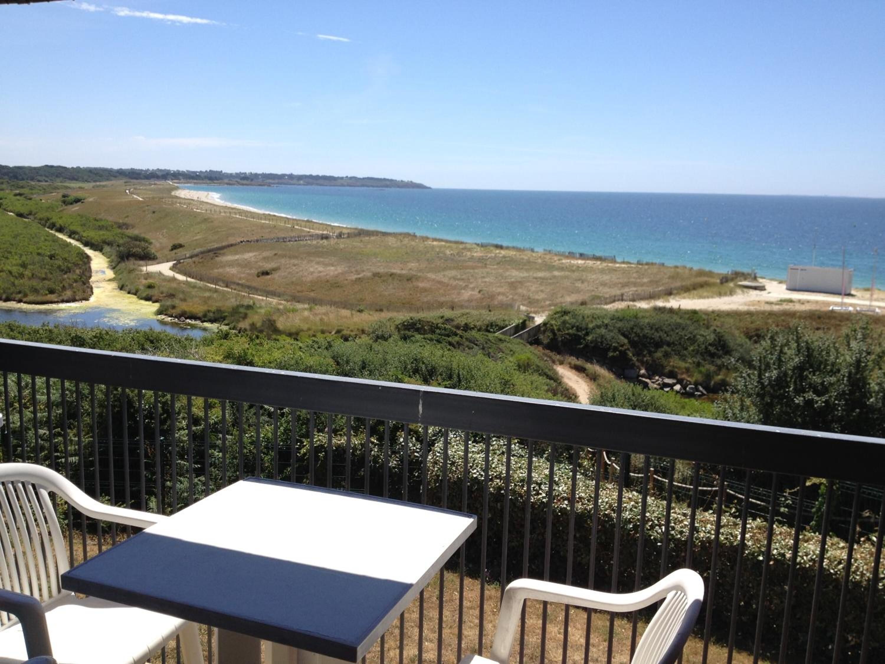 A balcony with a table and chairs overlooking a beach and a body of water.