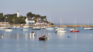 A marina with various boats docked, a lighthouse in the background, and a coastal town with buildings and trees. - Village Club Kerlannic (Arzon)