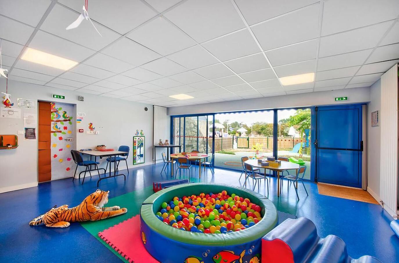 A brightly lit indoor play area with a ball pit, climbing wall, and a tiger plush toy on the floor.