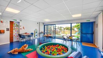 A brightly lit indoor play area with a ball pit, climbing wall, and a tiger plush toy on the floor.