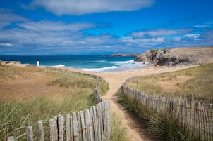 A coastal path leading to a beach with a wooden fence and grassy dunes.