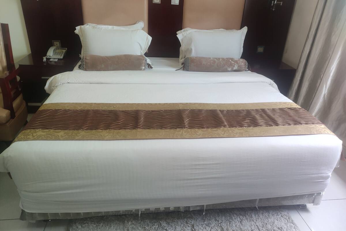 Quarto de hotel com uma cama grande, duas mesas de cabeceira, um telefone e uma mesinha de apoio.