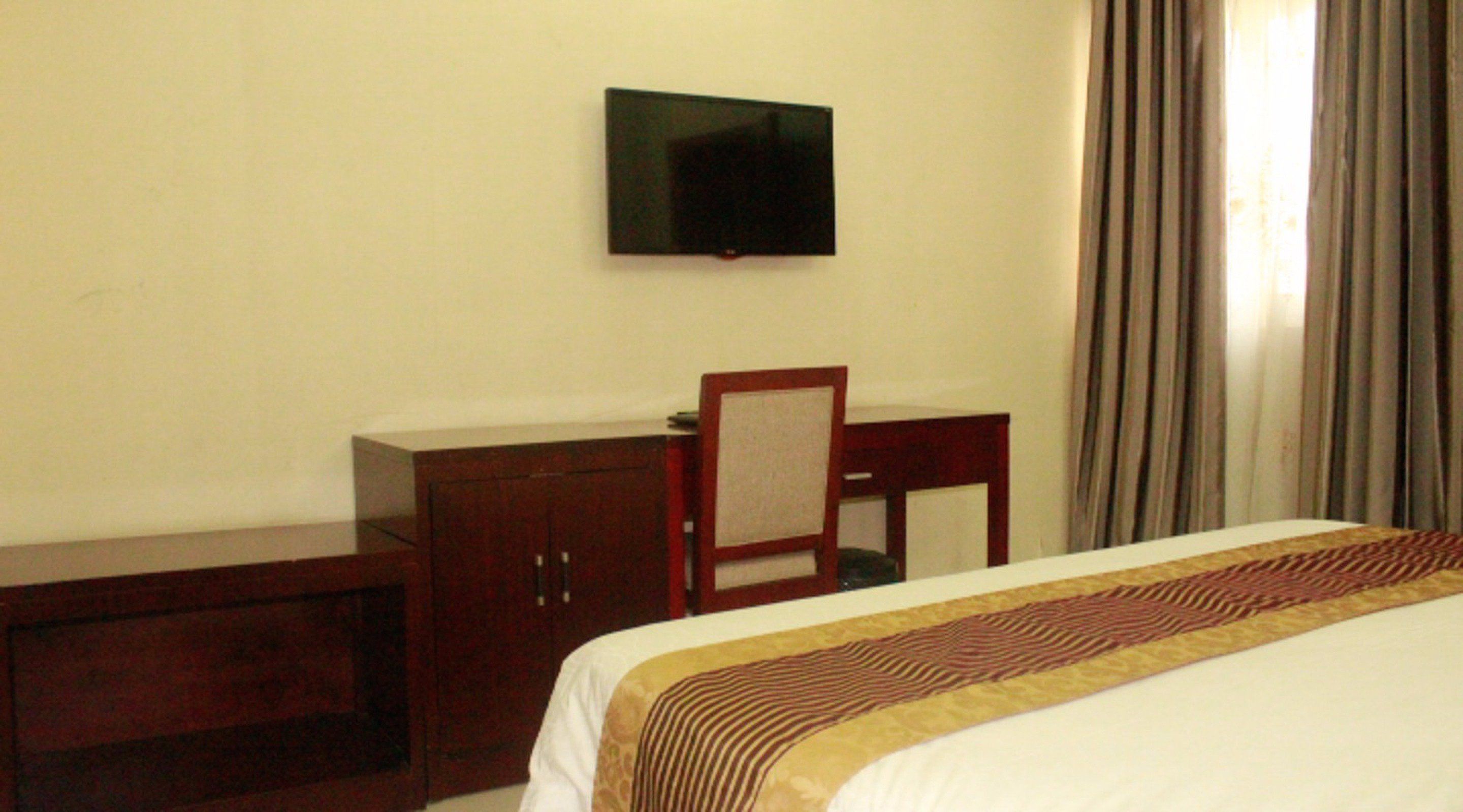 A hotel room with a bed, a desk, a chair, a television on the wall, and a window with curtains.