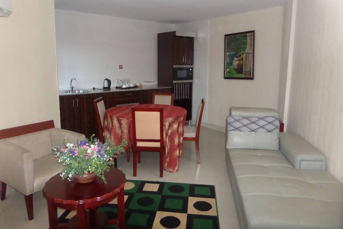 Uma sala de estar com sofá, uma mesa de jantar com cadeiras, uma cozinha e um quadro na parede.