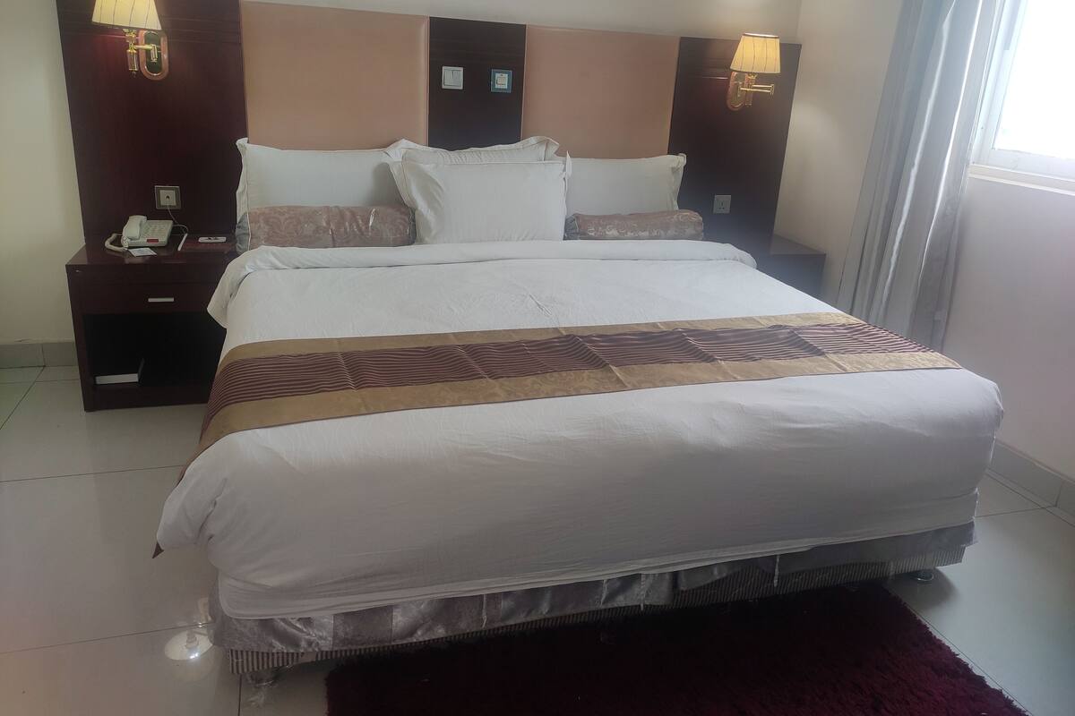 Uma cama bem arrumada com um cobreleira estampada, duas mesas de cabeceira com luminárias, e um telefone na mesa da esquerda.