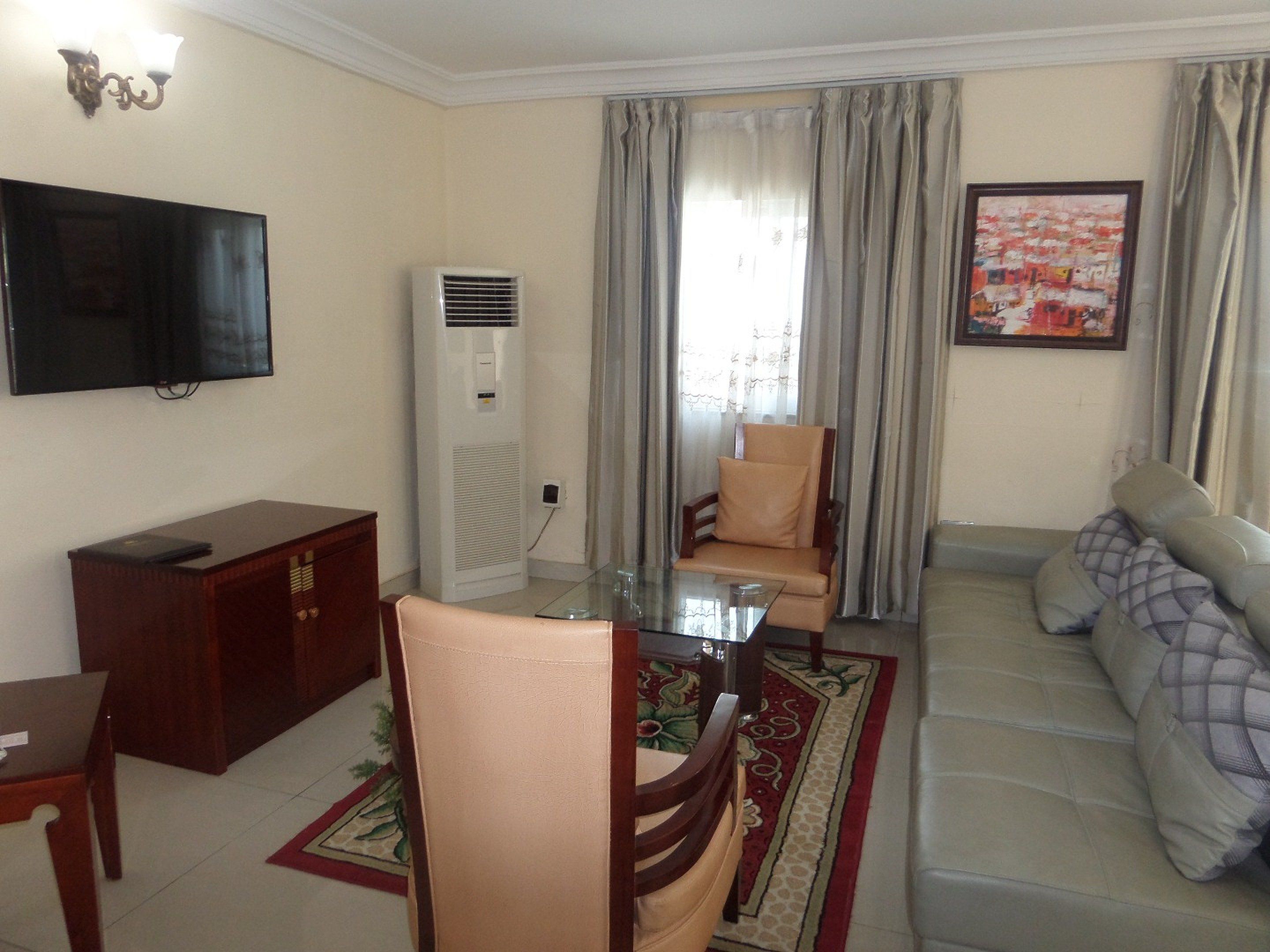 Uma sala de estar com sofá, mesa de centro de vidro, TV fixada na parede, ar condicionado e uma cadeira.