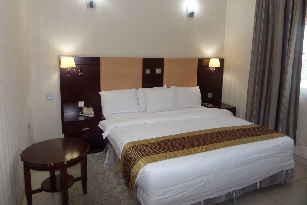 Quarto de hotel com uma cama grande, duas mesas de cabeceira e uma pequena escrivaninha.