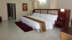 A hotel room with a large bed, a wooden headboard, a nightstand, a lamp, a painting on the wall, and a red rug.