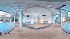 An indoor swimming pool with blue chairs and tables, ceiling fans, and a checkered ceiling pattern.