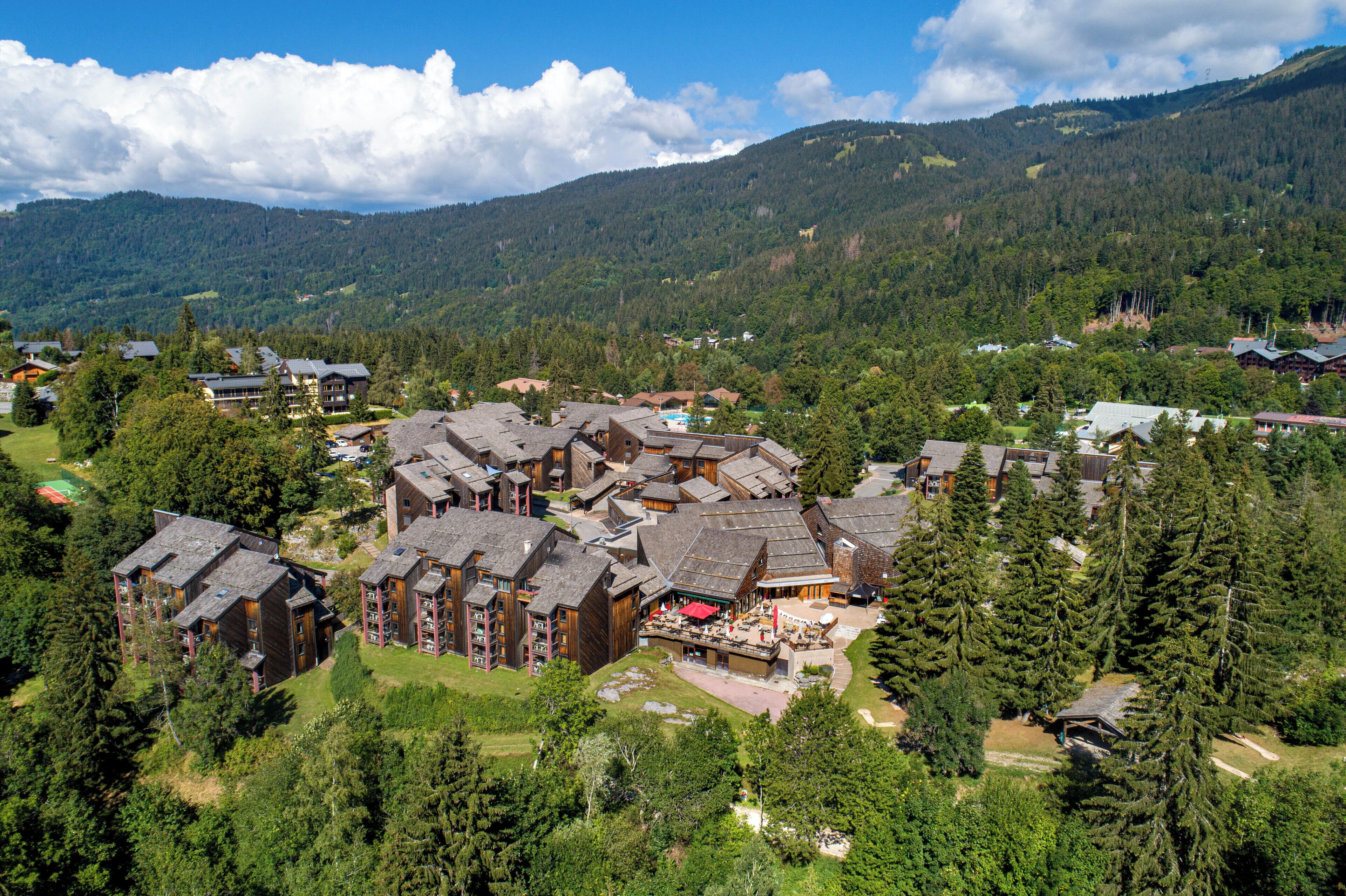 Un complexe hôtelier comprenant plusieurs bâtiments, une cour centrale et des collines boisées environnantes.