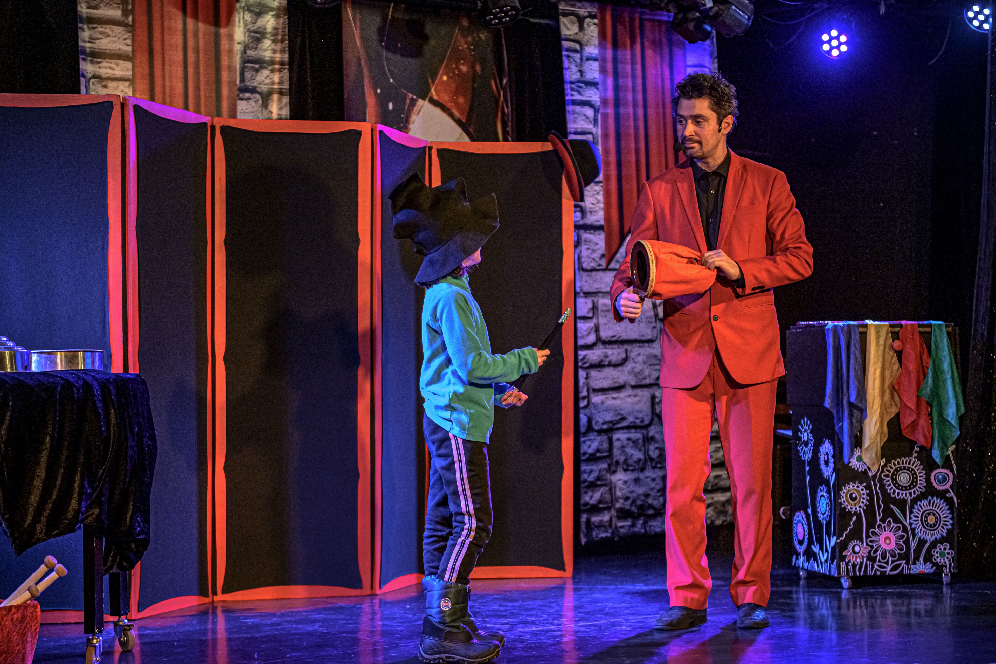 A stage with a performer in a red suit and a child in a blue outfit.