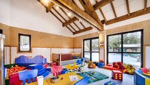 Une salle de jeux pour enfants aux couleurs vives, dotée d’un plafond haut et de grandes fenêtres.