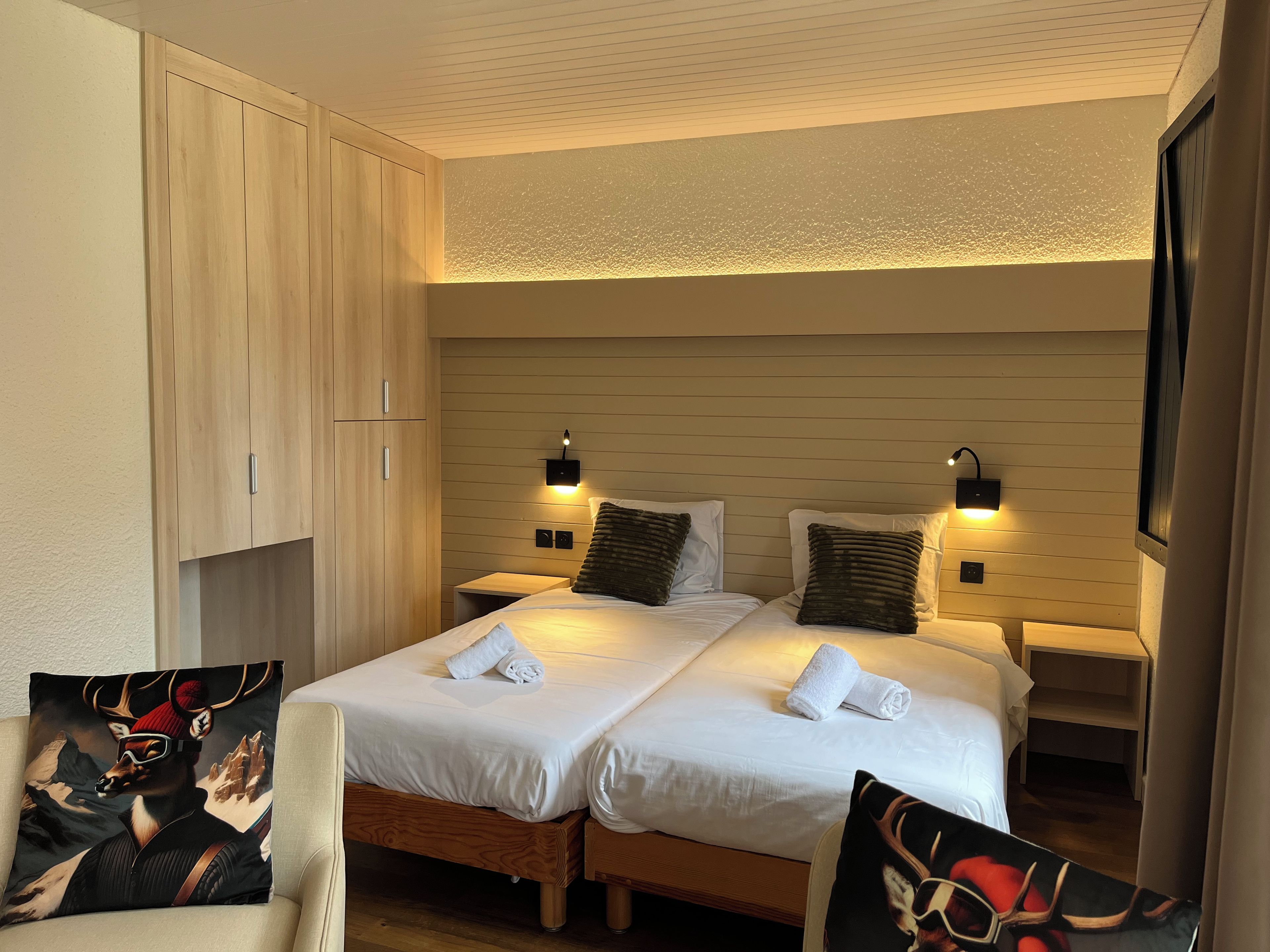 Un lit double avec du linge de lit blanc, deux tables de chevet avec des lampes, une armoire en bois et un téléviseur fixé au mur.