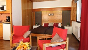 Una sala de estar acogedora con muebles de madera, una mesa de comedor con fruta y una cocina al fondo.