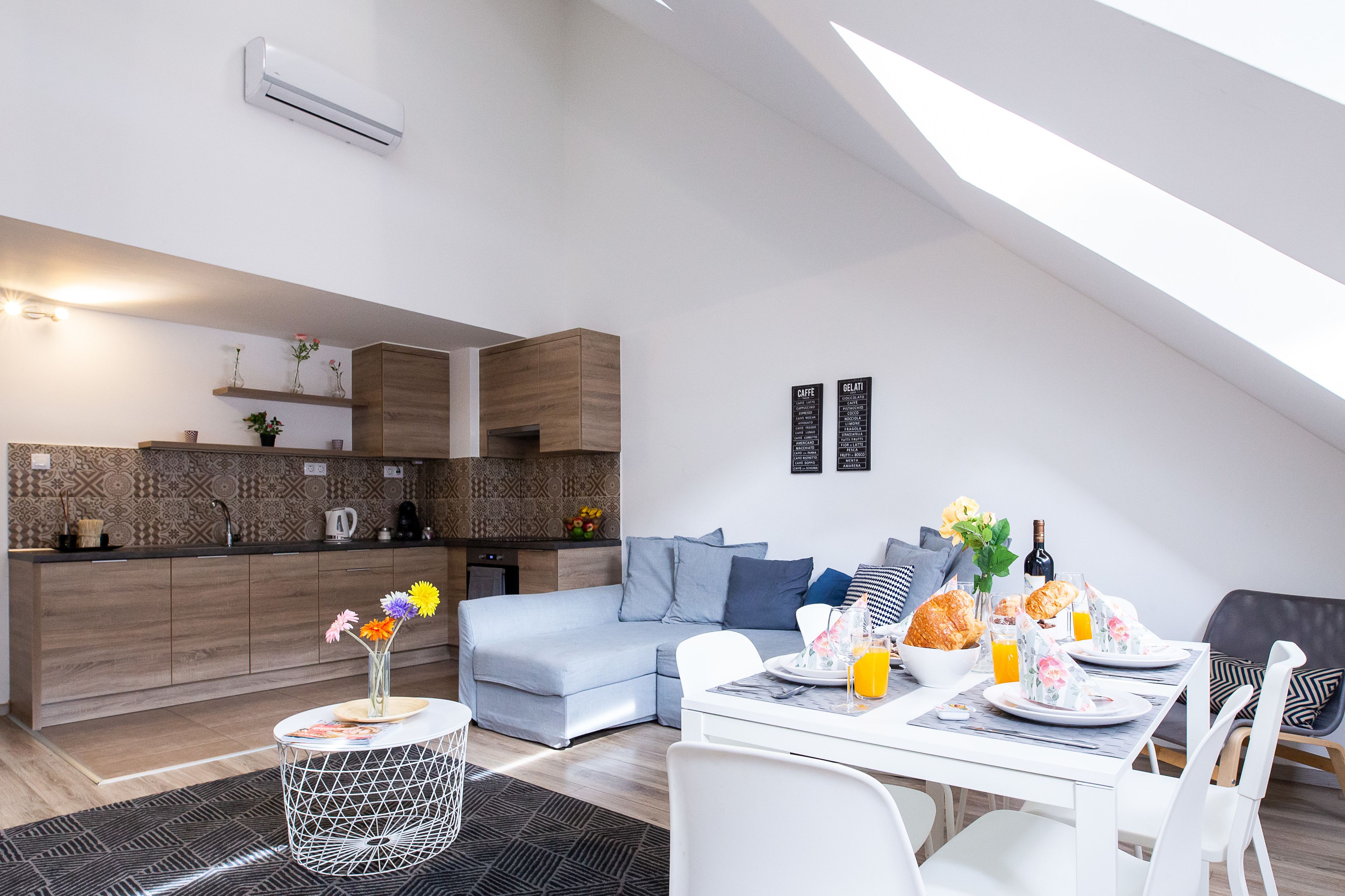 Une cuisine moderne dotée d’un four encastré, un coin repas avec une table et des chaises blanches, et un espace de vie comprenant un canapé et une table basse.