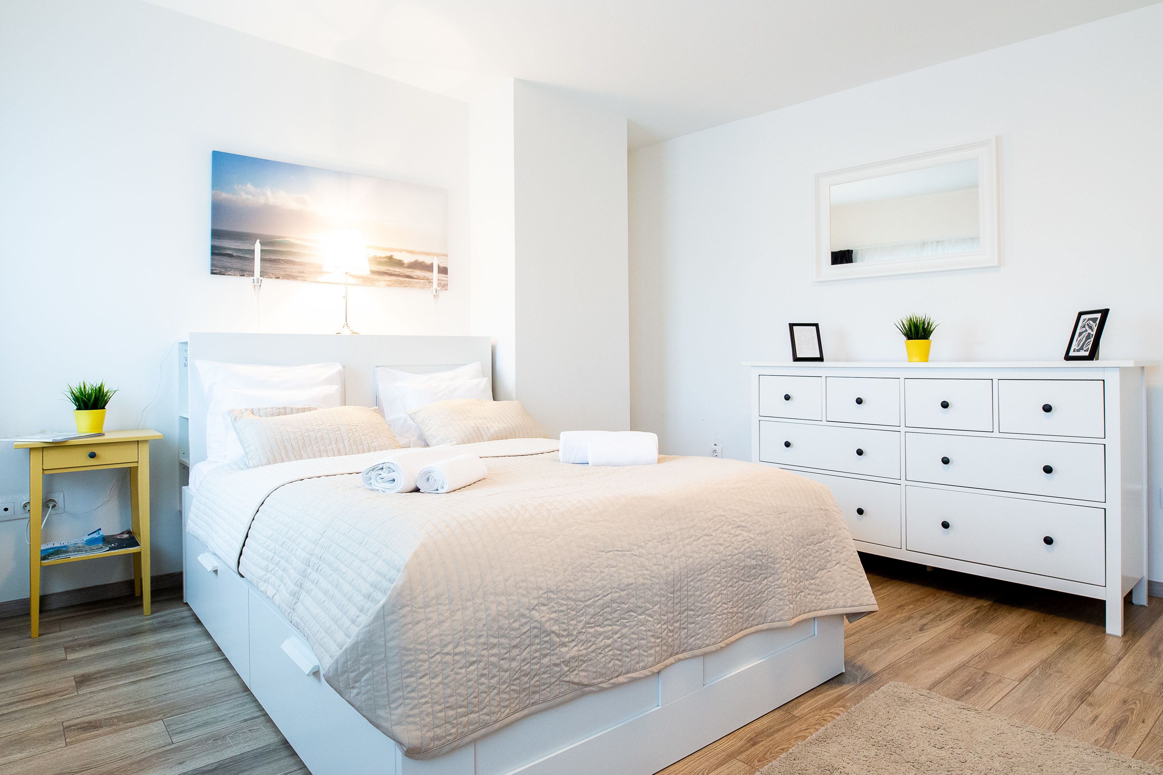 Quarto moderno com cama, mesa de cabeceira, cômoda e um quadro na parede.