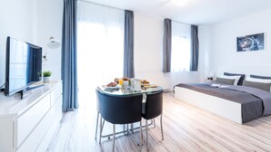 A modern hotel room with a bed, a TV, a dining table with chairs, and a large window with curtains. - Vagabond Corvin (Budapest)