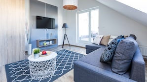 A modern living room with a grey sofa, a round coffee table, a TV mounted on the wall, and a large window providing natural light. - Vagabond Corvin (Budapest)