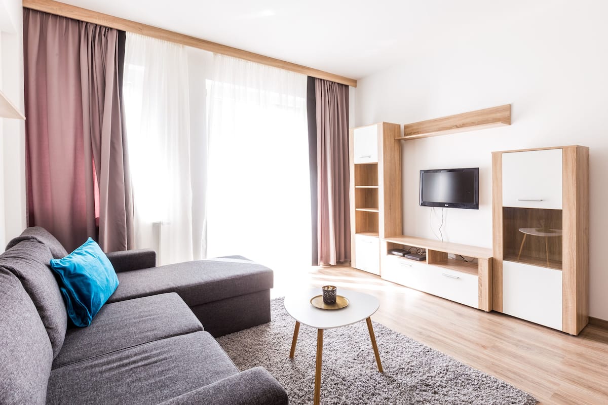 A modern living room with a grey sofa, a coffee table, a TV mounted on the wall, and a wooden cabinet.