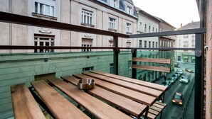A balcony with wooden benches and a metal bowl, overlooking a street with buildings and cars. - Vagabond Corvin (Budapest)