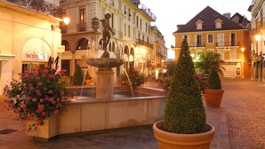 Ein Brunnen mit einer Statue in der Mitte, umgeben von Kübelpflanzen und Blumenkästen.