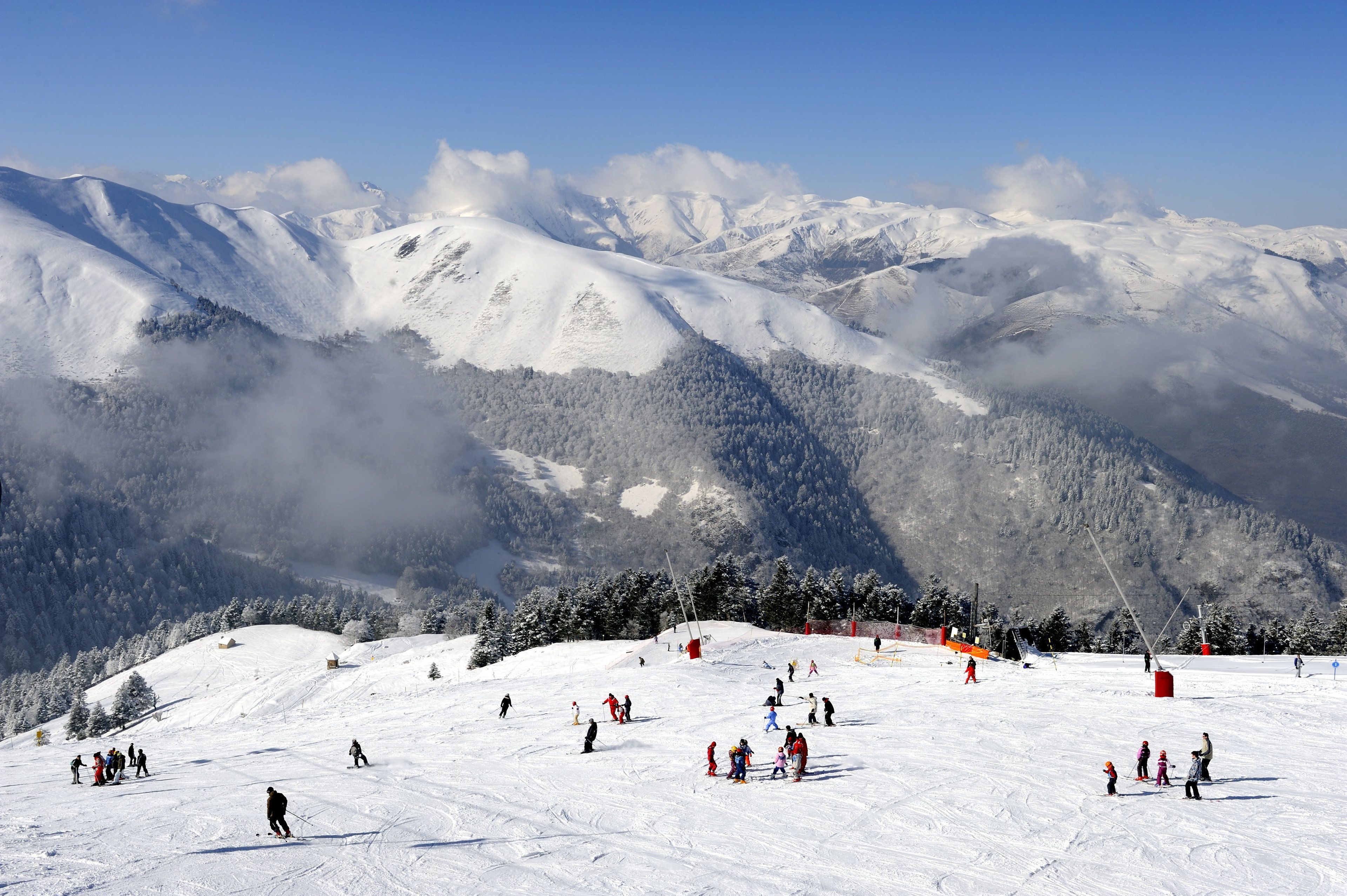 A snowy ski slope with skiers and snowboarders, surrounded by mountains and trees.