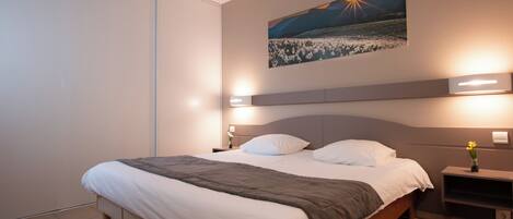 Una habitación de hotel moderna con una cama grande, mesitas de noche y un cuadro colgado en la pared.