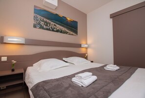 A hotel room with a bed, two bedside lamps, a nightstand with a vase of flowers, and a painting on the wall.