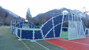 Un parque infantil con un aro de baloncesto y estructuras para escalar, con montañas al fondo.