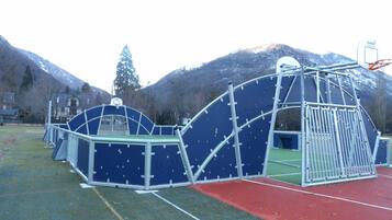 A playground with a basketball hoop and climbing structures, set against a backdrop of mountains.