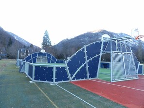 A playground with a basketball hoop and climbing structures, set against a backdrop of mountains.