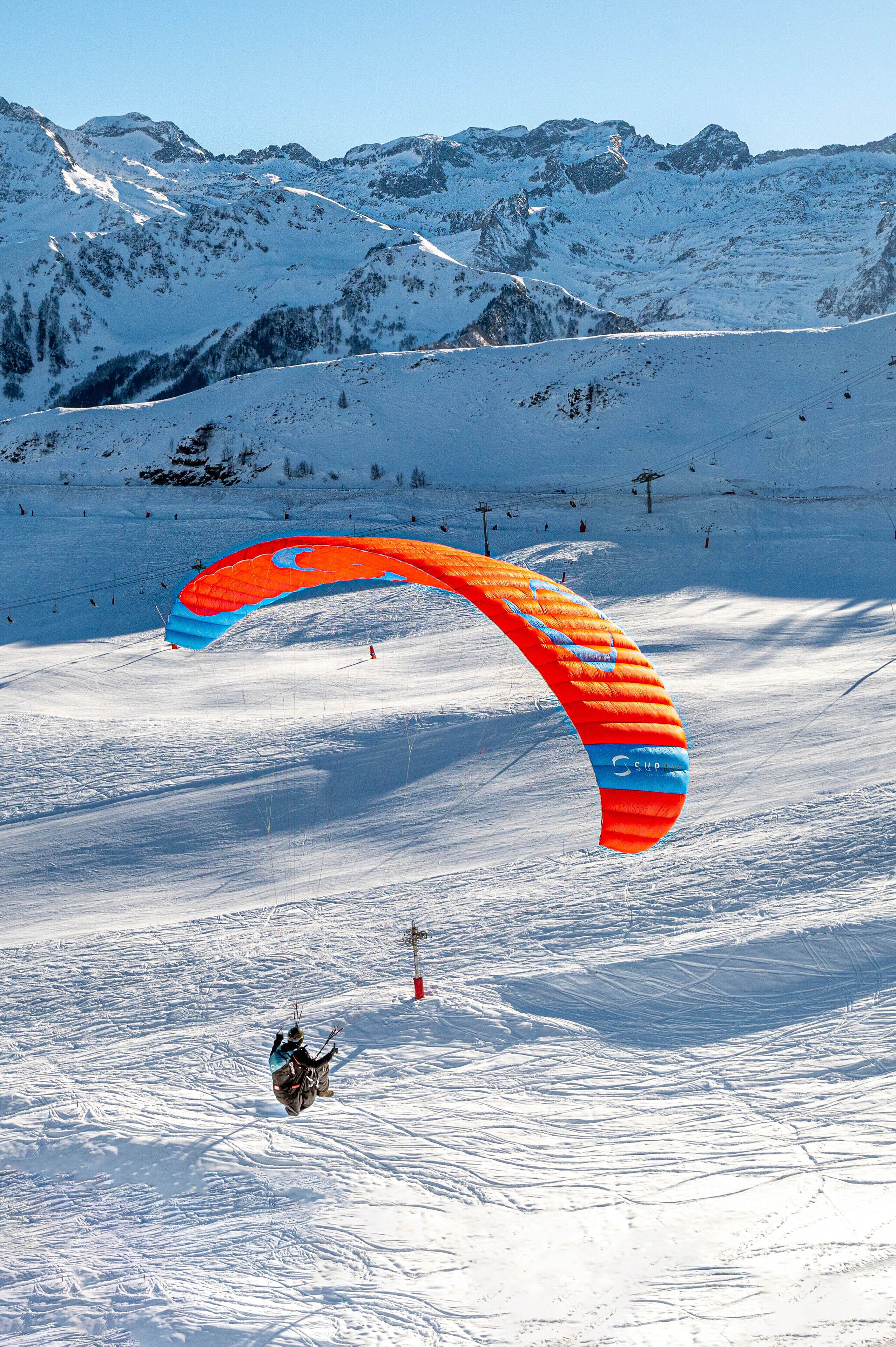 Un paysage de montagne enneigé où l'on voit une personne faire du parapente.