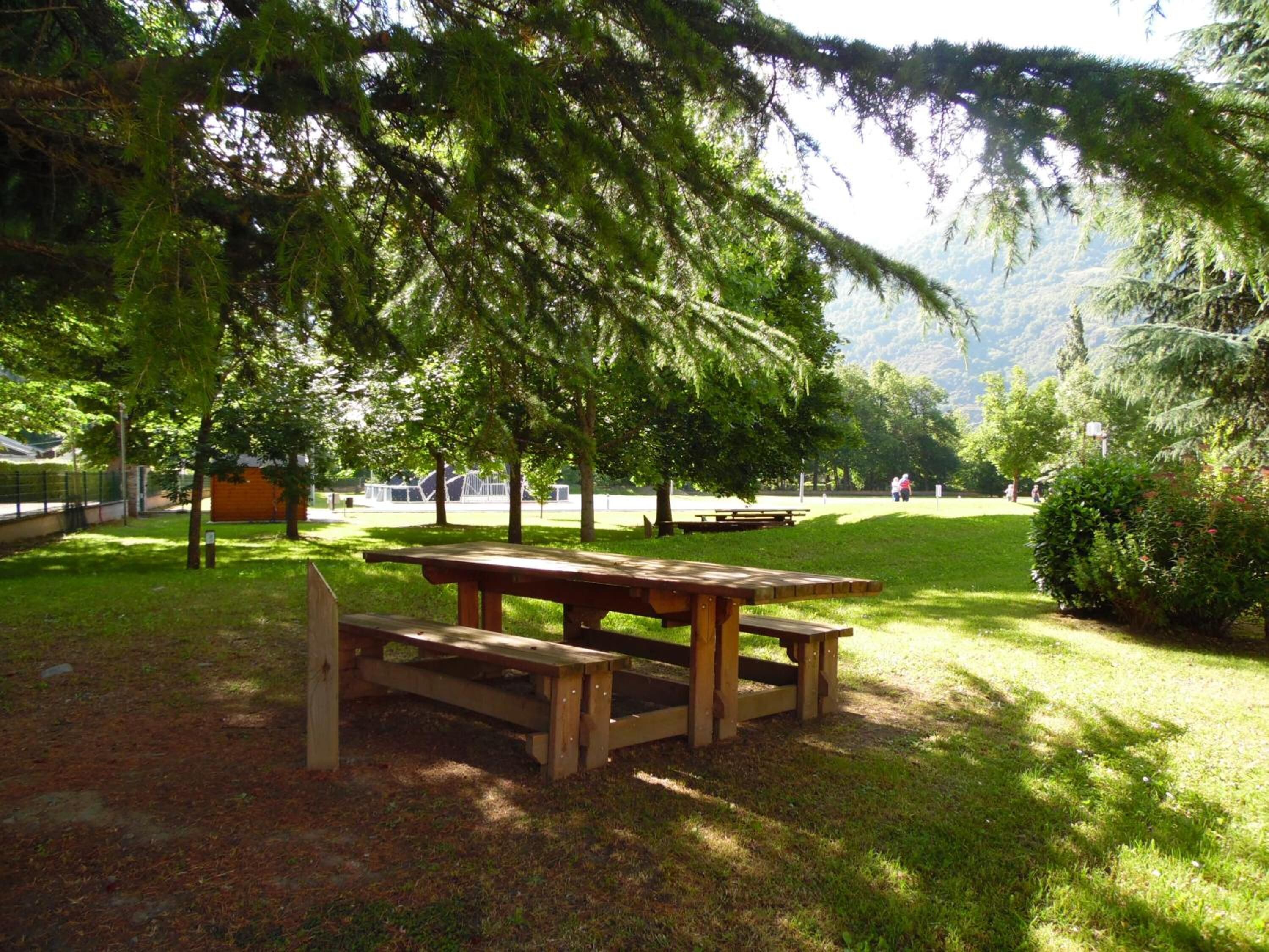 Un área de picnic con bancos y mesas de madera, rodeada de abundante vegetación y árboles.