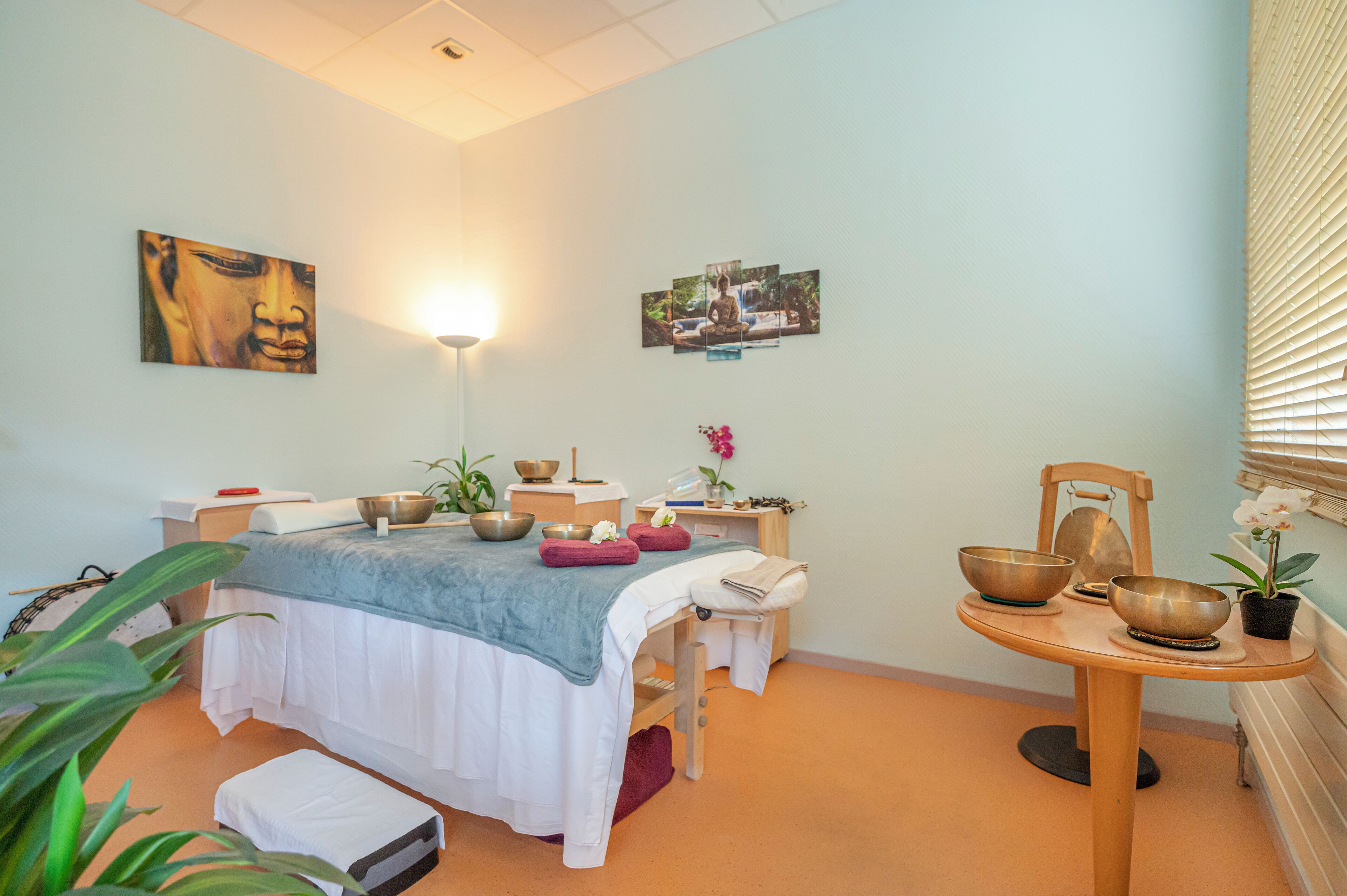 Una sala de spa con cama, camilla de masaje y una mesita baja con recipientes y una planta.