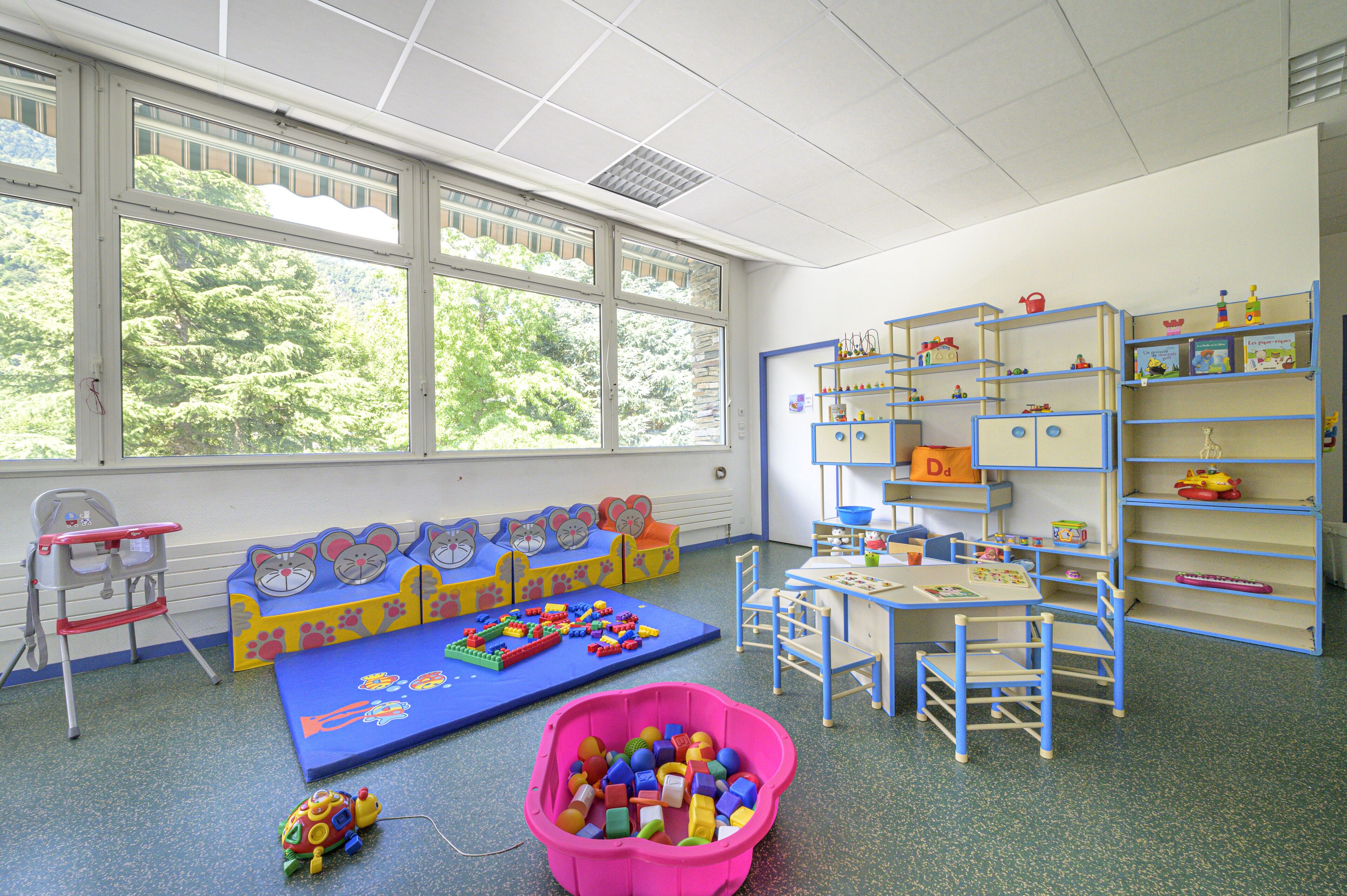 A children's playroom with a large window, play mats, toys, and shelves.